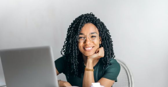 Online Reputation - Happy ethnic woman sitting at table with laptop