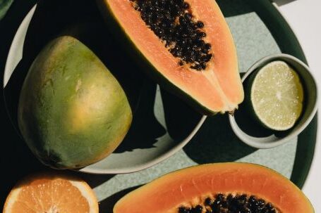 Efficient Layout. - Top view of halves of ripe papaya together with oranges and limes placed on green round dishes and green fabric on white background