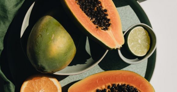 Efficient Layout. - Top view of halves of ripe papaya together with oranges and limes placed on green round dishes and green fabric on white background