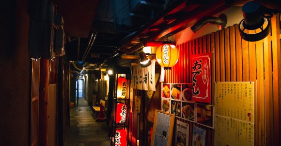 Bar Menu Tips - Narrow street with traditional Japanese izakaya bars decorated with hieroglyphs and traditional red lanterns in evening